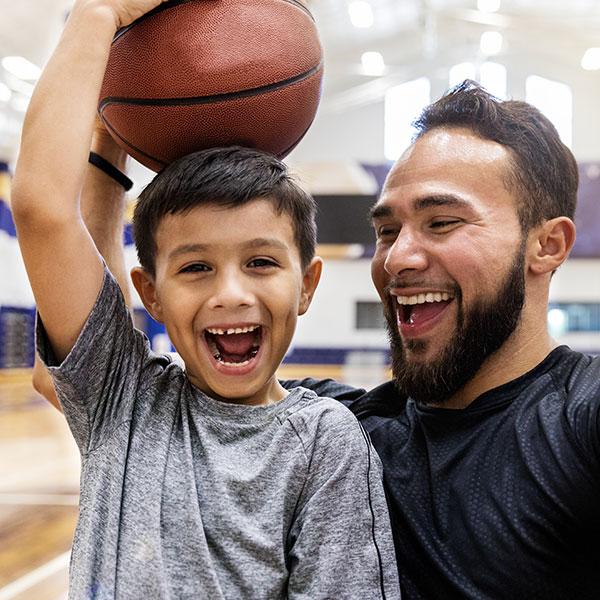 A father takes selfie while his son holds a basketball on his head.