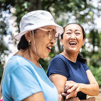 A mother and her adult daughter enjoy a laugh as they walk out on a sunny day.