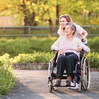 An elderly woman in a wheelchair enjoys a sunny day outside.