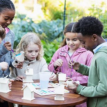 Des enfants prennent plaisir à peindre en plein air une cabane à oiseaux artisanale.