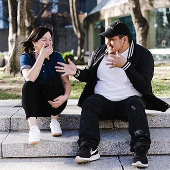 Friends have a funny conversation outside on a set of concrete steps.