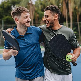 Two men smiling as they leave a pickleball court.