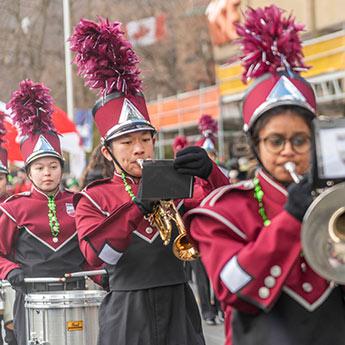 Young people in uniforms play in a marching band with a Canadian flag in the background.