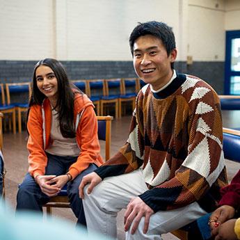 Young people share stories while sitting in a circle of chairs in a large room.