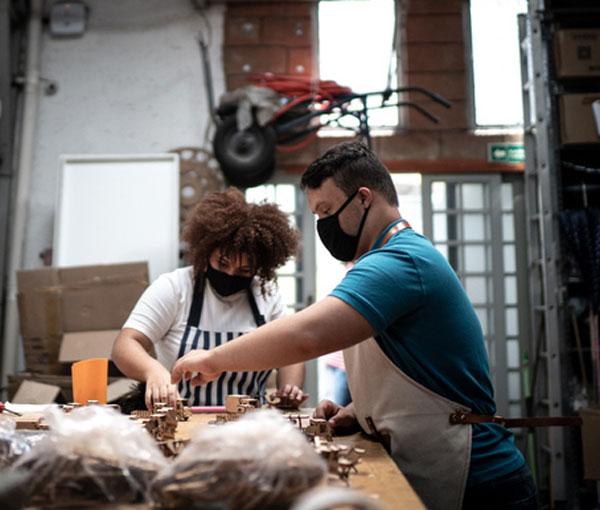 Coworkers checking some wooden toys, both wearing face masks.