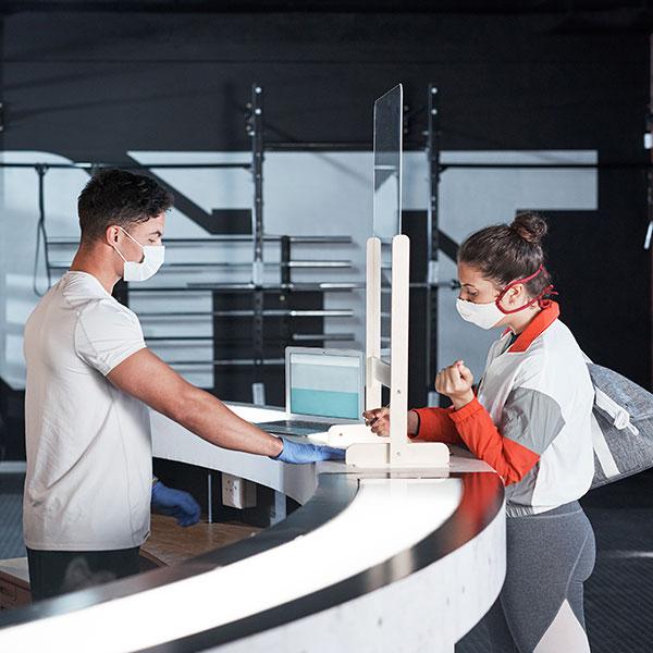 Two people standing at a reception desk who are wearing masks