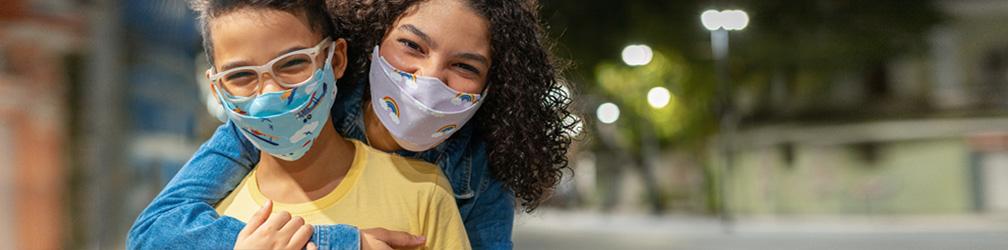 Two youth wearing respiratory masks and holding each other outdoors.