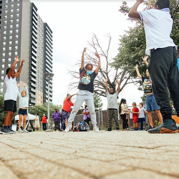 Des jeunes forment un cercle à l’extérieur d’un immeuble de grande hauteur pour faire des activités physiques. 