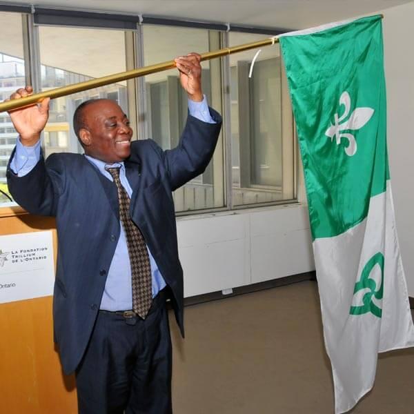 Un homme debout devant une estrade tient le drapeau franco-ontarien au-dessus de sa tête.