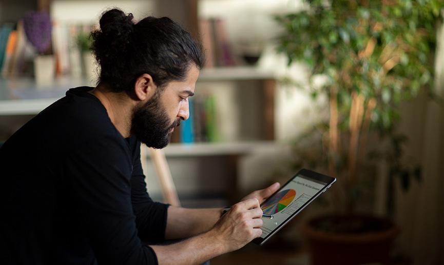 A person sitting indoors is using a tablet to look at data and analytics in a pie chart.