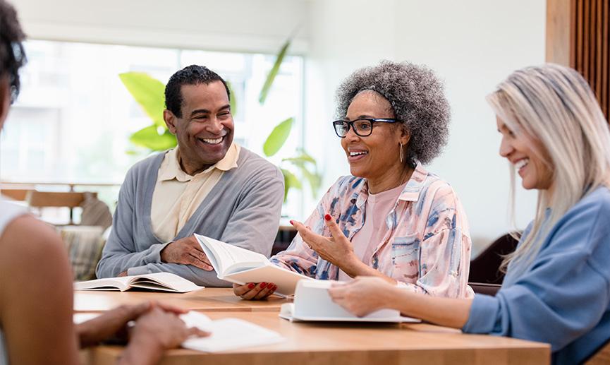 A group of adults gather around a table for a book club meeting  