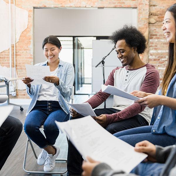 A small group of happy people are reading a script inside a studio.  