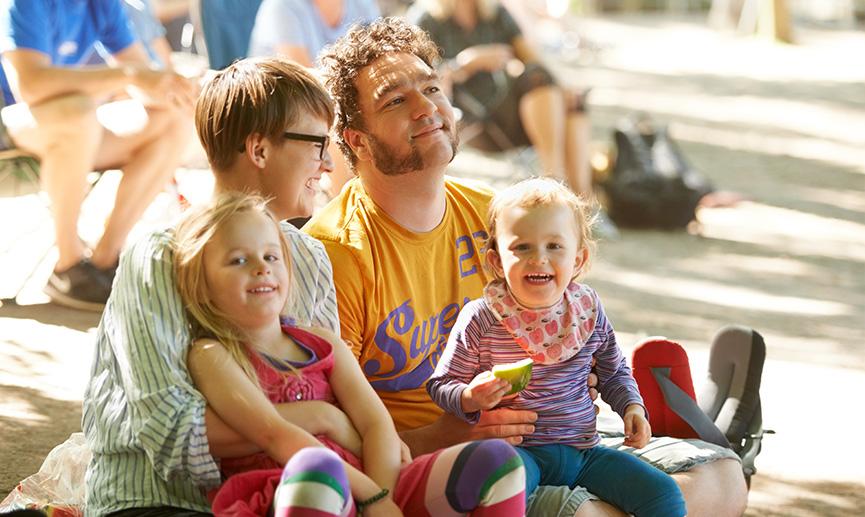 A young family of four sitting down to enjoy the bands at an outdoors music festival