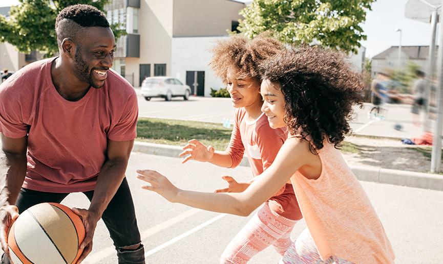 Two teenagers playing basketball outside with an adult.