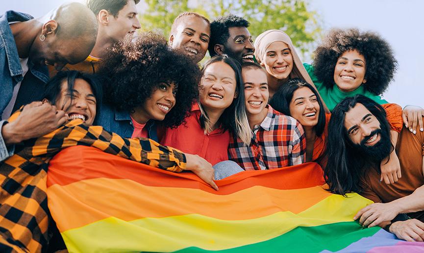 Diverses personnes joyeuses tiennent un drapeau de la Fierté en plein air