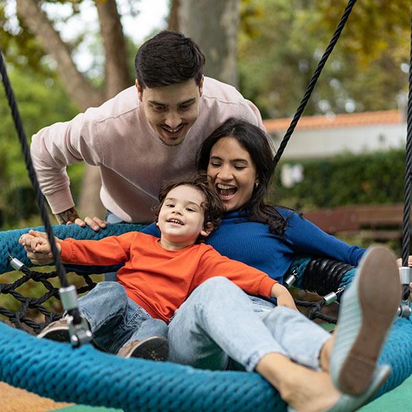 A family plays with an accessible swing at an outdoor playground.
