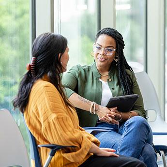 Two women have a formal discussion in an office lobby.