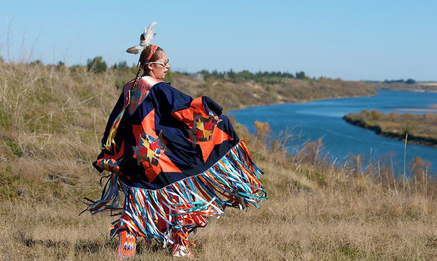 A woman in a jingle dress performs a traditional Indigenous dance.
