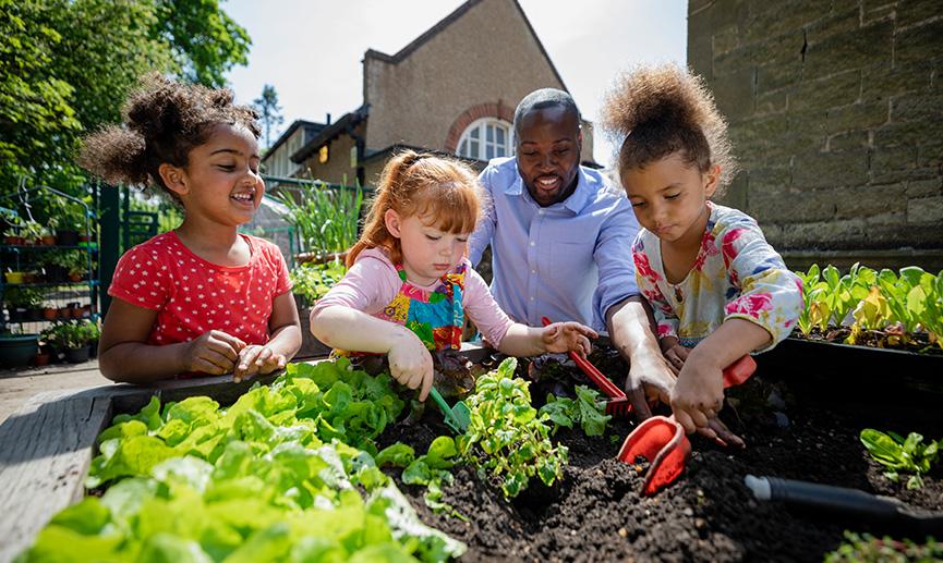 A group of kids planting in a garden with an adult.