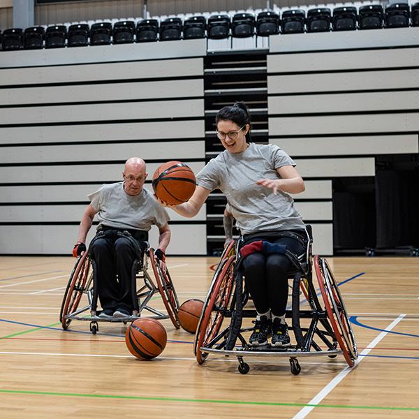 A team of wheelchair basketball players are laughing and dribbling a basketball on a sports court.