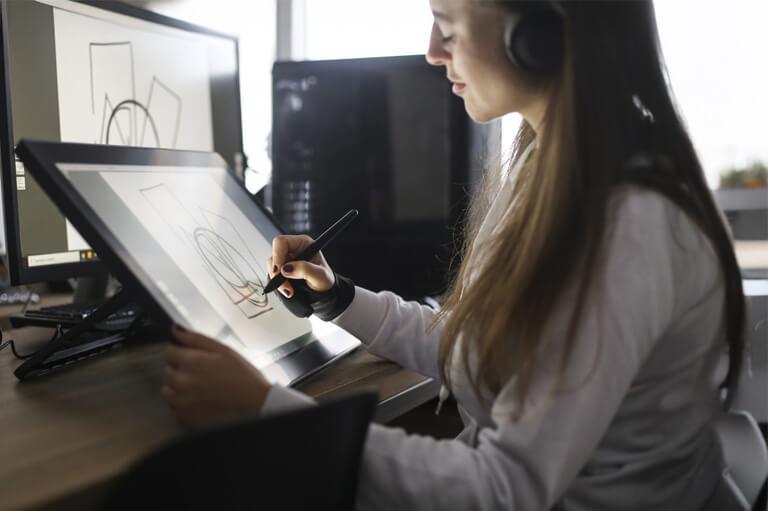 Person using a digital pen to draw on a graphics tablet beside a computer monitor.