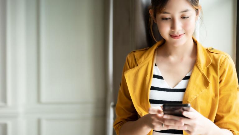   A woman is smiling as she uses her phone.