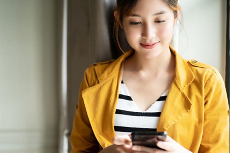 A woman is smiling as she uses her phone.