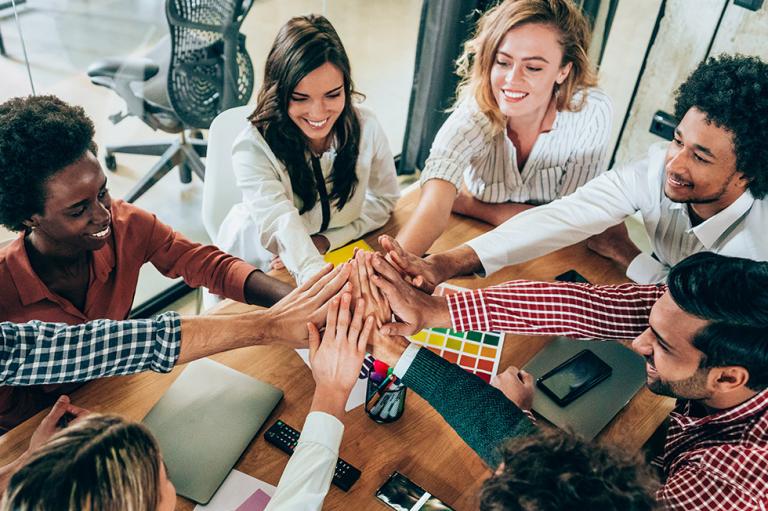 Group of people sitting at a table smiling and giving a high five.