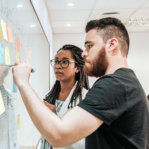 Two people are brainstorming and writing ideas on sticky notes.