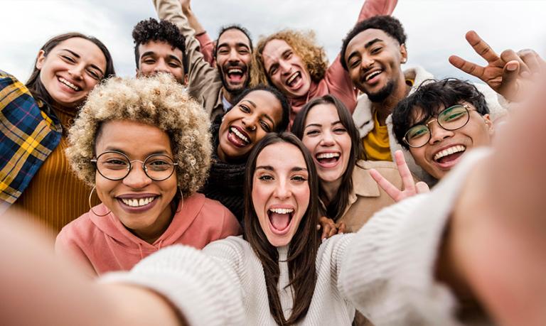 A group of multiracial friends take a picture of themselves smiling at the camera.