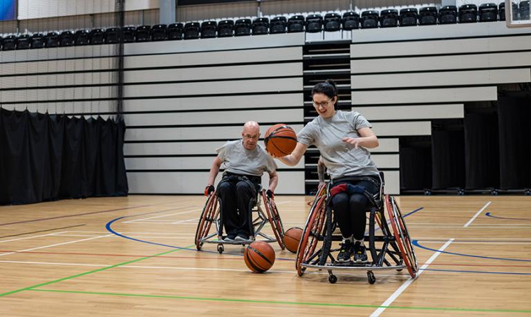 Des joueurs de basketball en fauteuils roulants rient et driblent sur un terrain de sports.