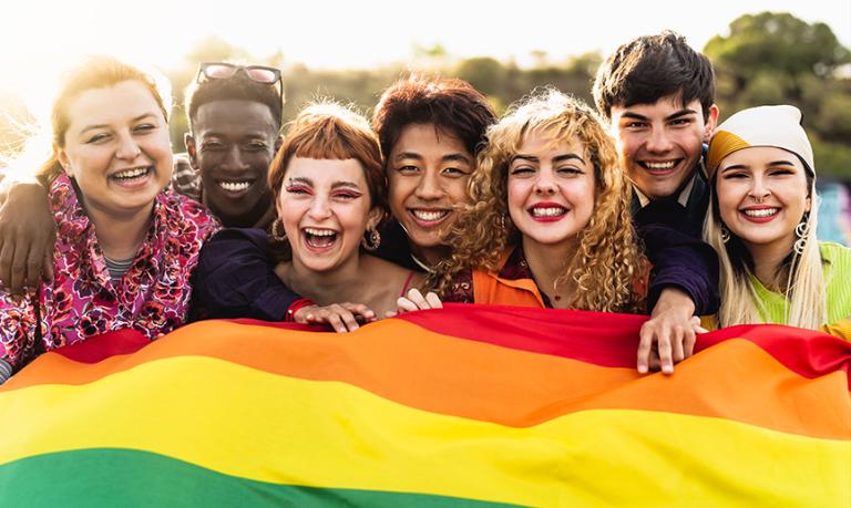 Happy young diverse friends celebrating Pride and holding a rainbow flag.