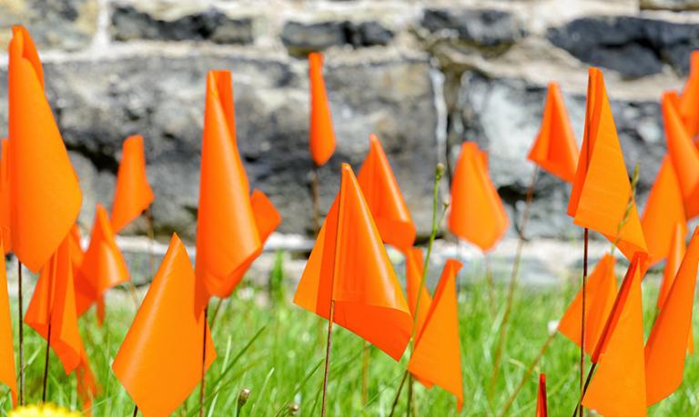 De petits drapeaux orange plantés dans l’herbe en mémoire des milliers d’enfants autochtones disparus dans le système des pensionnats au Canada.