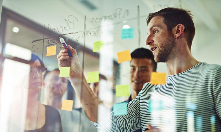 A team brainstorming around a glass board with notes and sticky tabs.
