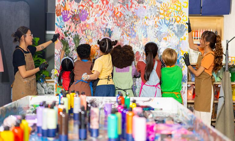 School children learning acrylic art on canvas frame workshop with teacher at art studio.