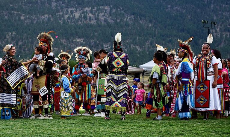 Indigenous dancers dressed in regalia gather before the dancing begins.